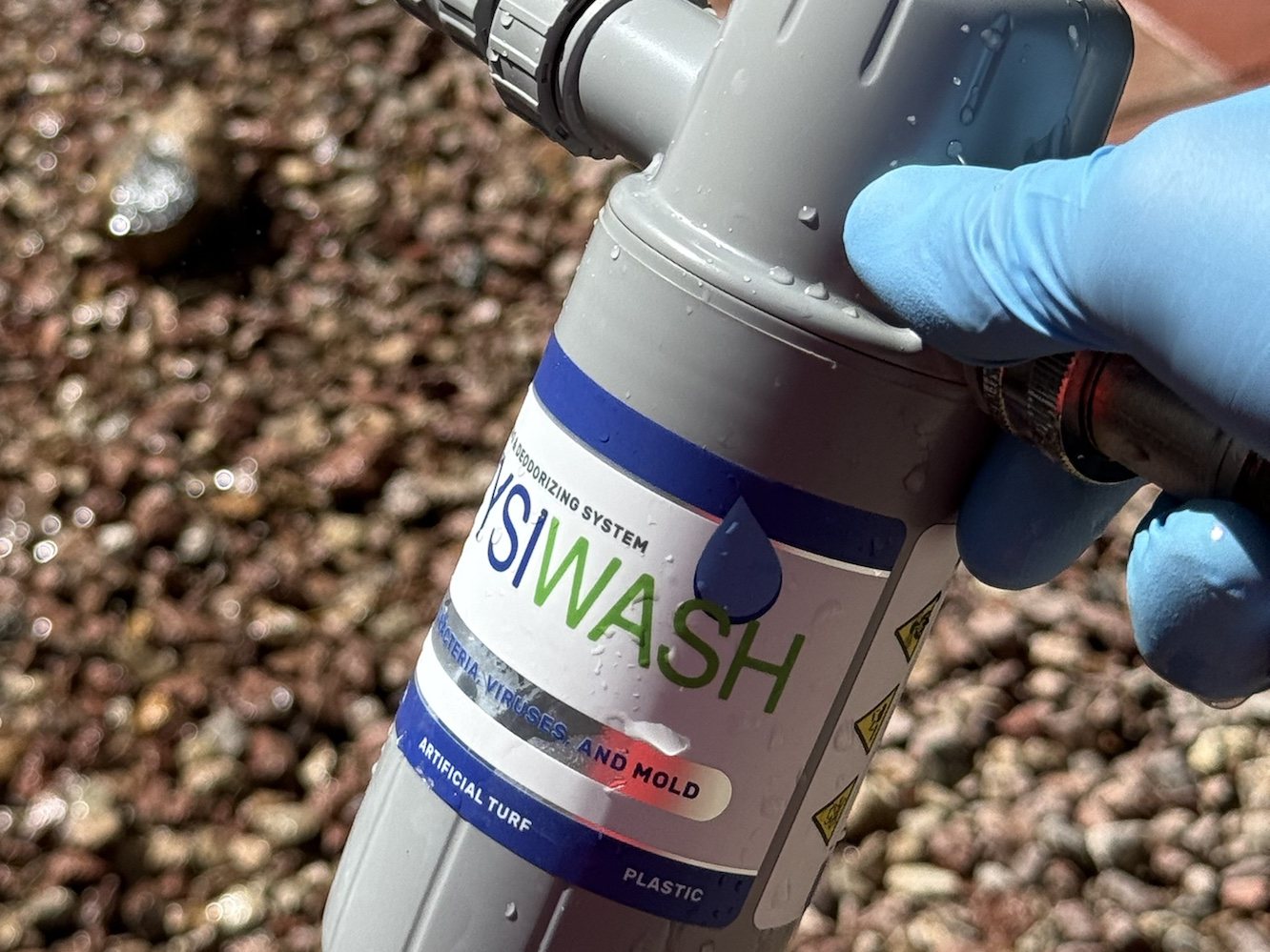 Close-up of the Wysiwash hose-end sanitizing unit used by Poop Scoop Dude, manufacturer label listing bacteria, viruses and mold, and artificial turf and plastic surfaces