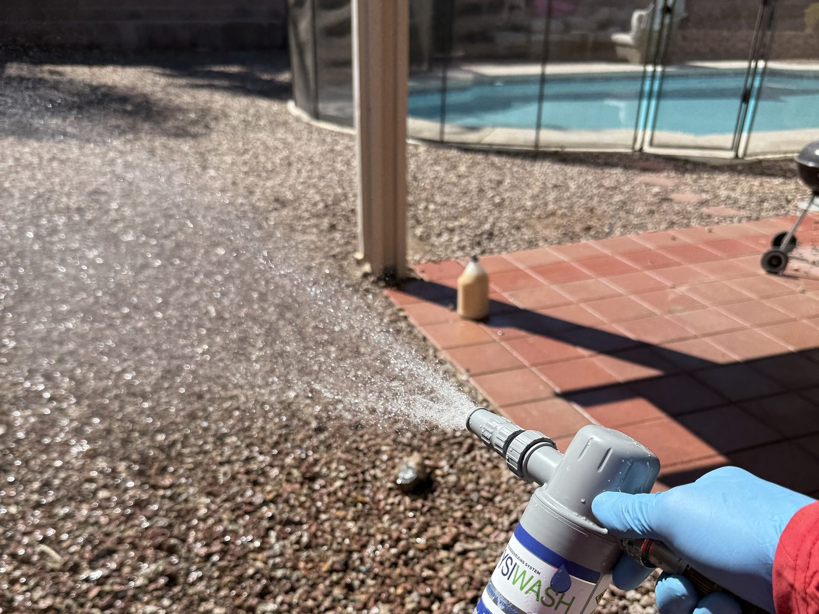 Applying Wysiwash sanitizer across a Las Vegas backyard with a hose end sprayer, pool and patio behind